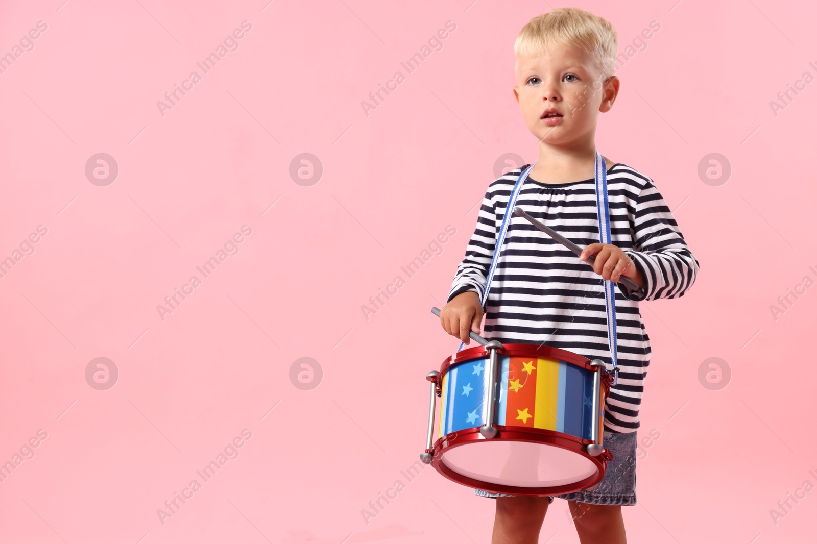 Photo of Cute little boy playing drum on pink background. Space for text