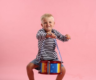 Photo of Cute little boy playing drum on pink background