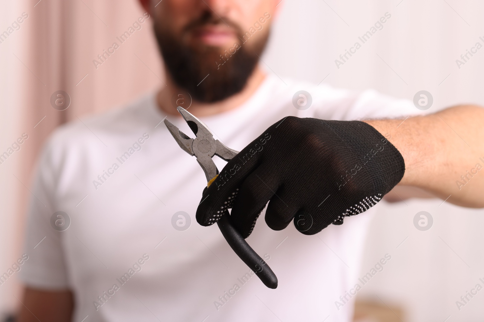 Photo of Man in glove holding pliers indoors, closeup