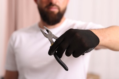 Photo of Man in glove holding pliers indoors, closeup