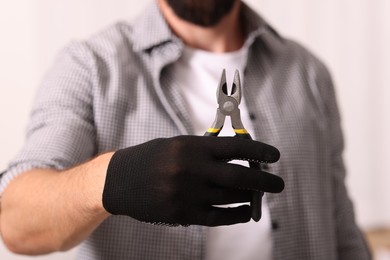Photo of Man in glove holding pliers indoors, closeup