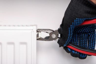 Photo of Man fixing heating radiator with pliers indoors, closeup