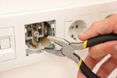 Photo of Man fixing power sockets with pliers indoors, closeup