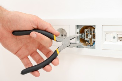 Photo of Man fixing power sockets with pliers indoors, closeup