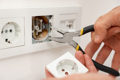 Photo of Man fixing power sockets with pliers indoors, closeup