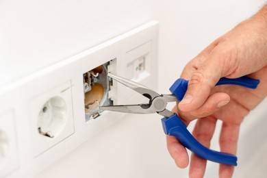 Photo of Man fixing power sockets with pliers indoors, closeup
