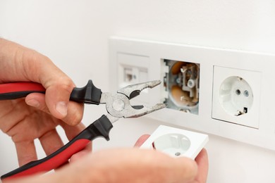 Photo of Man fixing power sockets with pliers indoors, closeup