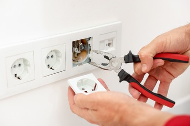 Photo of Man fixing power sockets with pliers indoors, closeup