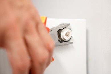 Photo of Man fixing heating radiator with pliers indoors, closeup
