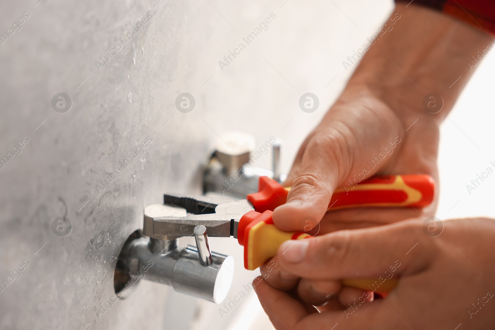 Photo of Man fixing water valve with pliers indoors, closeup