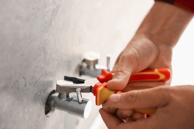 Photo of Man fixing water valve with pliers indoors, closeup