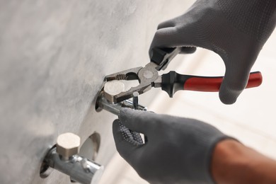 Photo of Man fixing water valve with pliers indoors, closeup