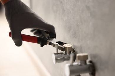 Photo of Man fixing water valve with pliers indoors, closeup