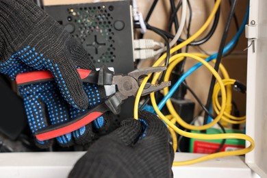 Photo of Man fixing heating radiator with pliers indoors, closeup