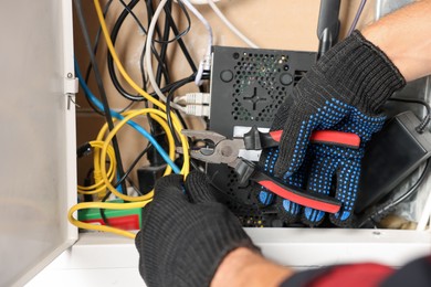 Photo of Man fixing heating radiator with pliers indoors, closeup