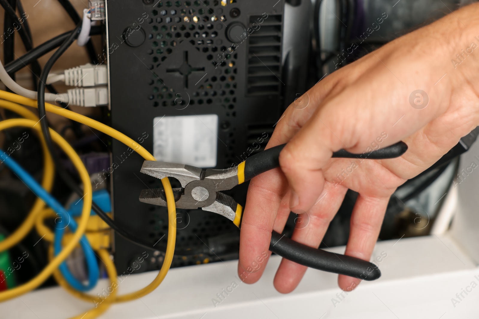 Photo of Man fixing heating radiator with pliers indoors, closeup