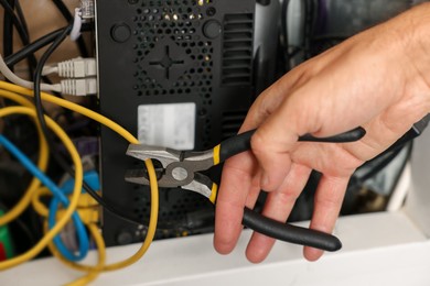 Photo of Man fixing heating radiator with pliers indoors, closeup