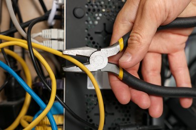 Photo of Man fixing heating radiator with pliers indoors, closeup