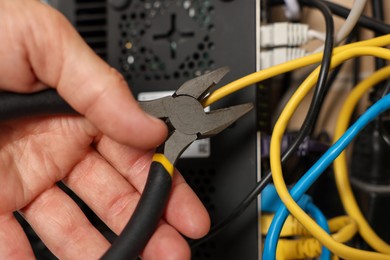 Photo of Man fixing heating radiator with pliers indoors, closeup