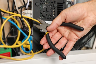 Photo of Man fixing heating radiator with pliers indoors, closeup