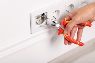 Photo of Man fixing power sockets with pliers indoors, closeup