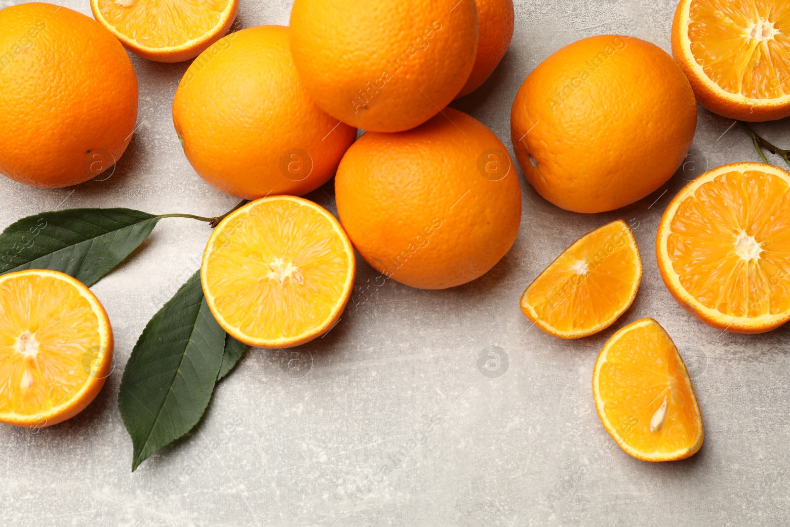 Fresh ripe oranges and green leaves on grey table, flat lay Photo of Fresh ripe oranges and green leaves on grey table, flat lay