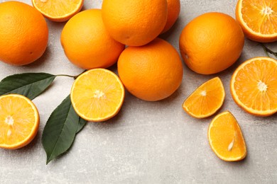 Photo of Fresh ripe oranges and green leaves on grey table, flat lay