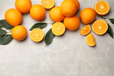 Photo of Fresh ripe oranges and green leaves on grey table, flat lay. Space for text