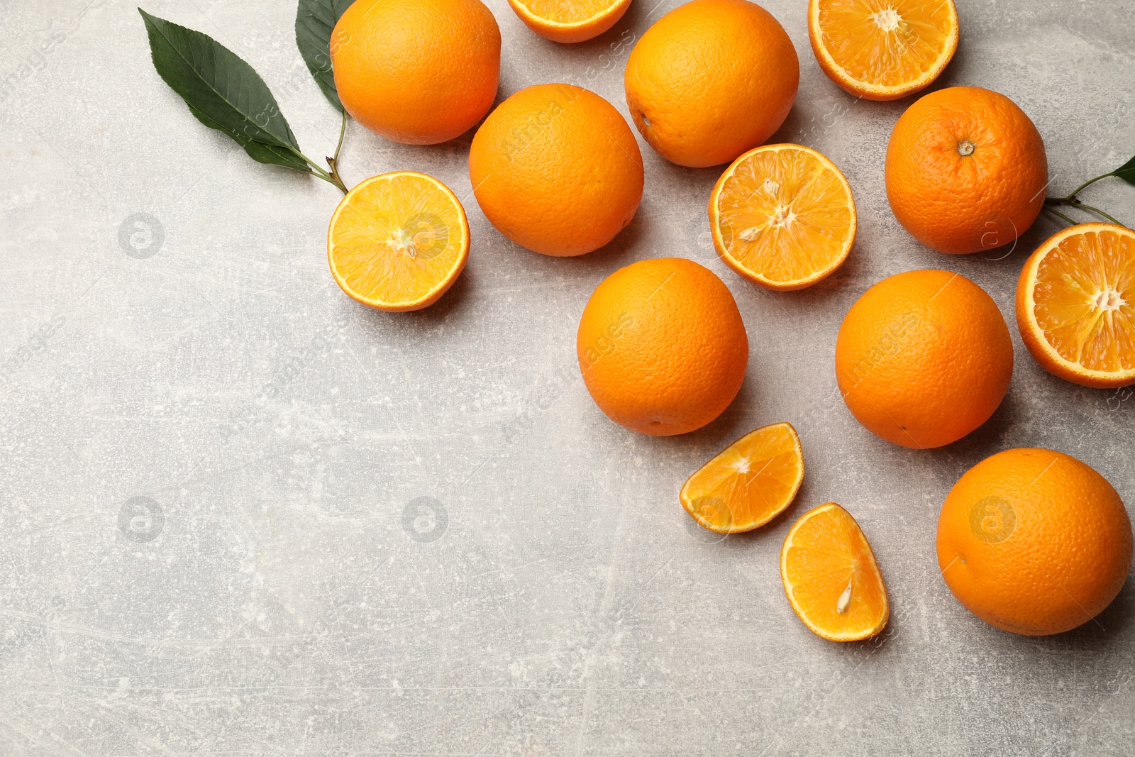 Fresh ripe oranges and green leaves on grey table, flat lay. Space for text Photo of Fresh ripe oranges and green leaves on grey table, flat lay. Space for text