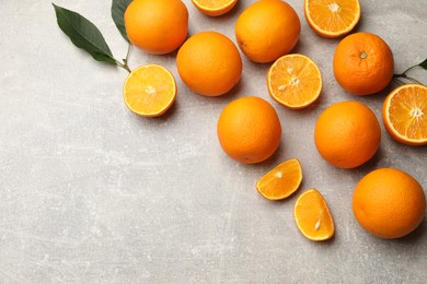 Photo of Fresh ripe oranges and green leaves on grey table, flat lay. Space for text