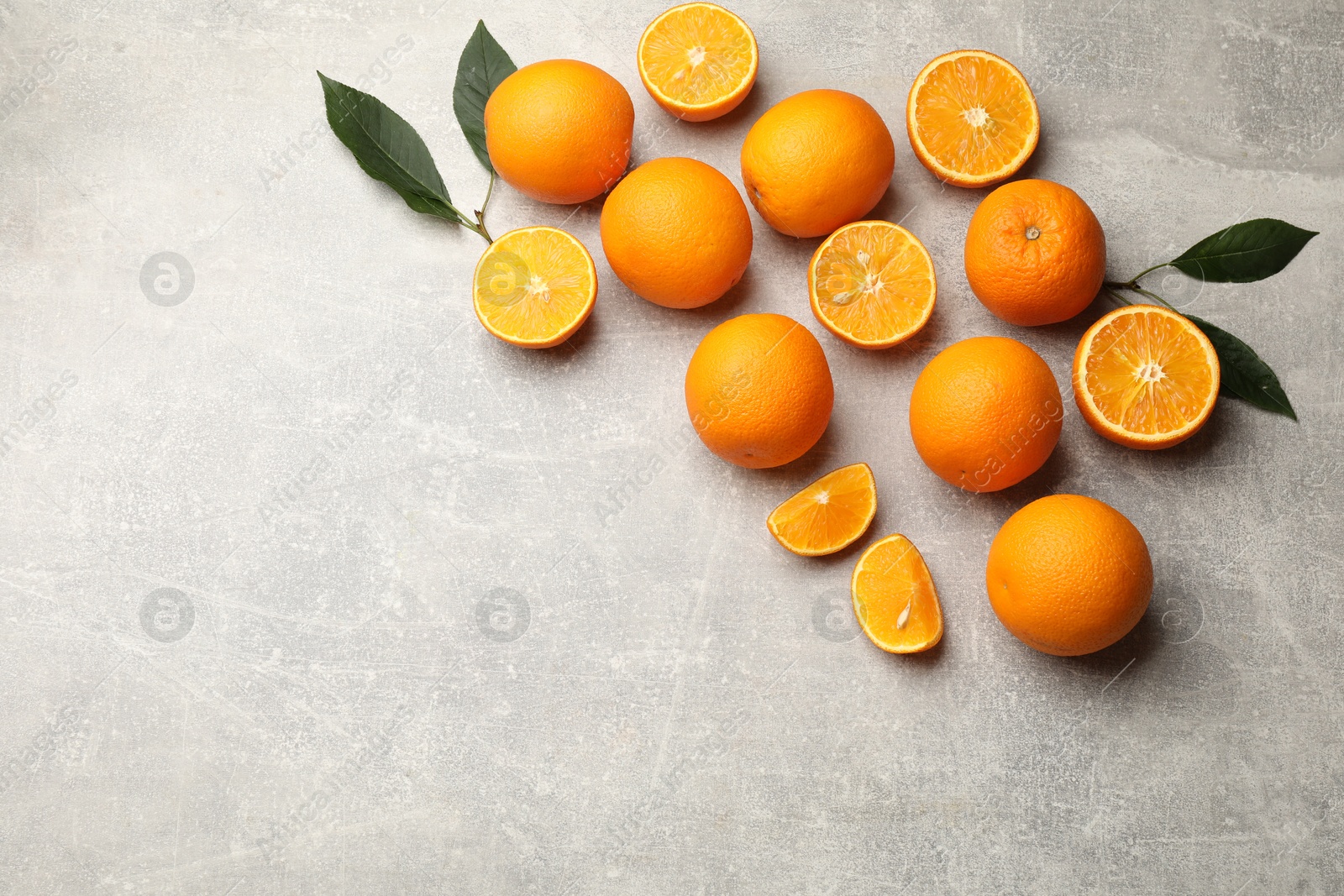 Fresh ripe oranges and green leaves on grey table, flat lay. Space for text Photo of Fresh ripe oranges and green leaves on grey table, flat lay. Space for text