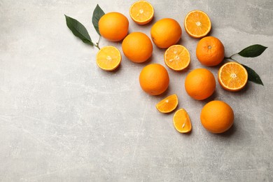 Photo of Fresh ripe oranges and green leaves on grey table, flat lay. Space for text