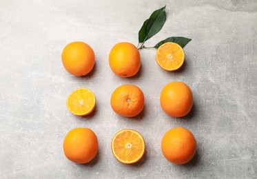 Photo of Fresh ripe oranges and green leaves on grey table, flat lay
