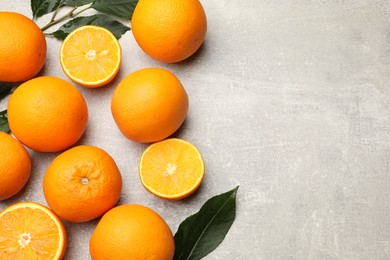 Photo of Fresh ripe oranges and green leaves on grey table, flat lay. Space for text