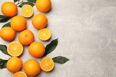 Photo of Fresh ripe oranges and green leaves on grey table, flat lay. Space for text