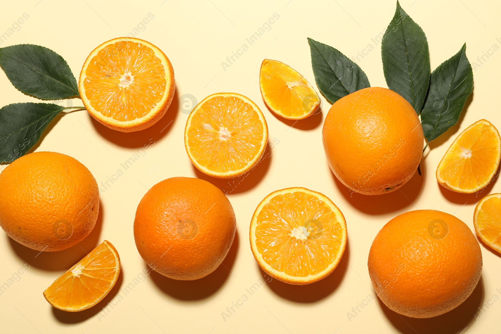 Photo of Fresh ripe oranges and green leaves on beige background, flat lay