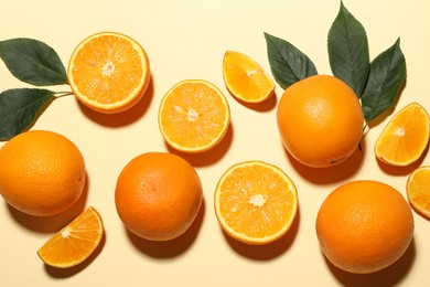 Photo of Fresh ripe oranges and green leaves on beige background, flat lay