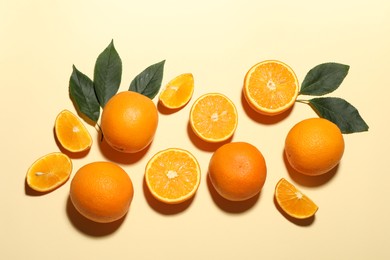 Photo of Fresh ripe oranges and green leaves on beige background, flat lay