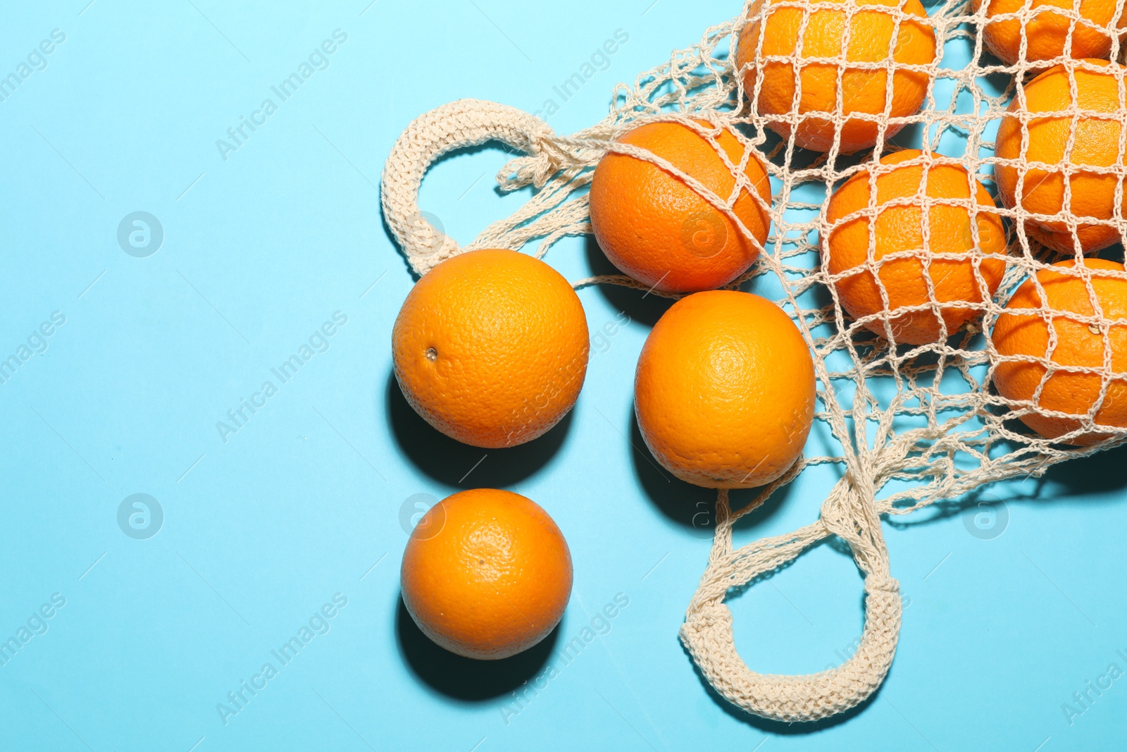 Fresh ripe oranges and string bag on light blue background, flat lay. Space for text Photo of Fresh ripe oranges and string bag on light blue background, flat lay. Space for text