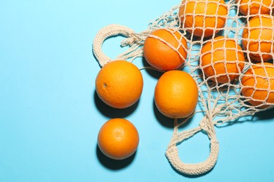 Photo of Fresh ripe oranges and string bag on light blue background, flat lay. Space for text