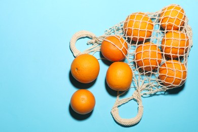 Photo of Fresh ripe oranges and string bag on light blue background, flat lay. Space for text