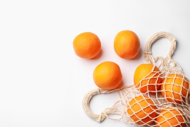 Photo of Fresh ripe oranges and string bag on white background, flat lay. Space for text
