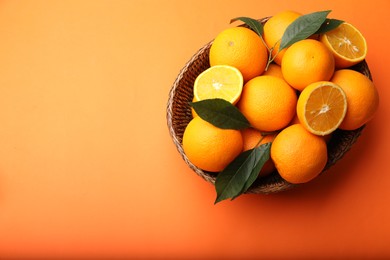 Photo of Fresh ripe oranges and green leaves in wicker basket on orange background, top view. Space for text
