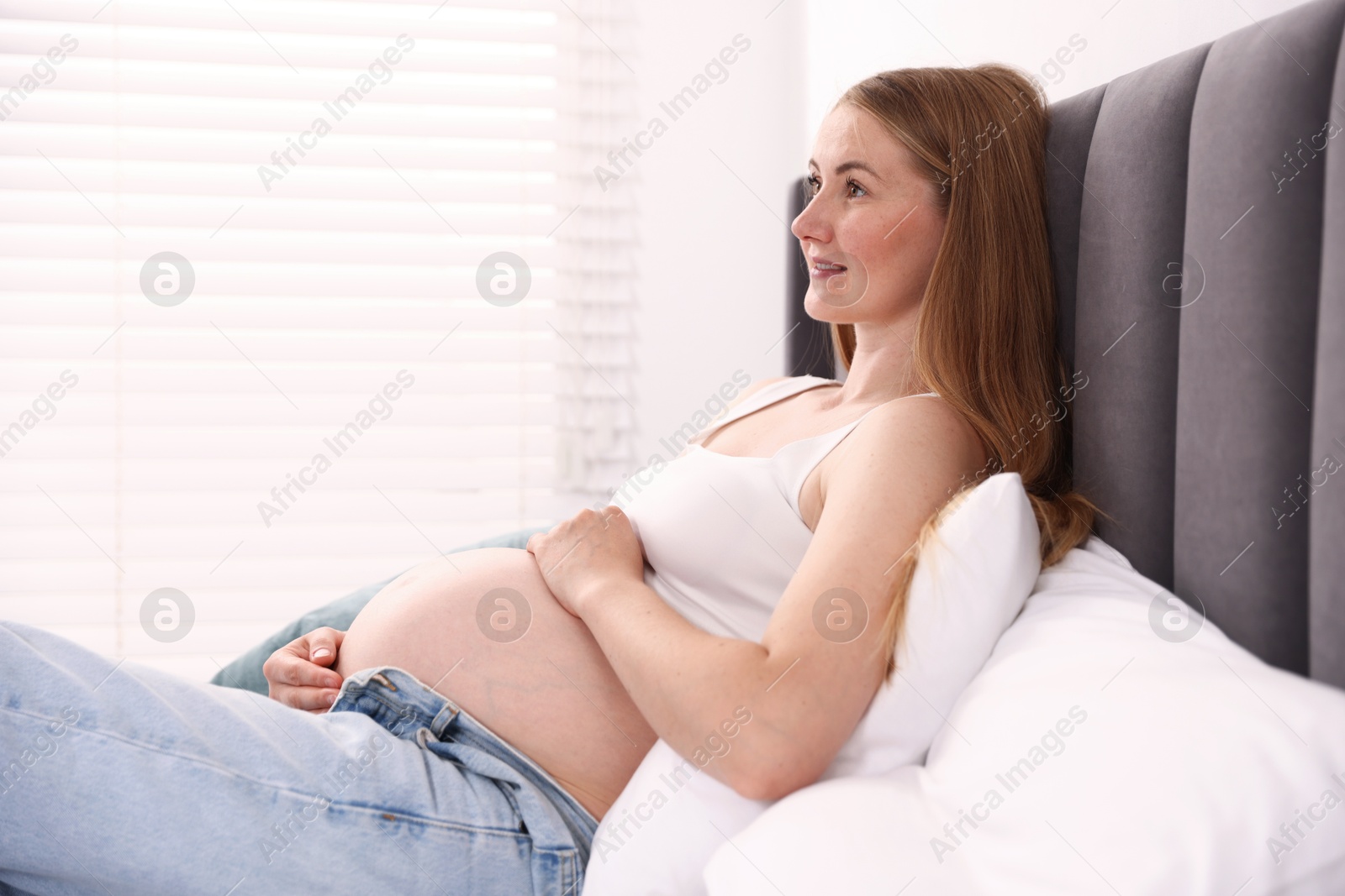 Photo of Beautiful pregnant woman on bed at home. Space for text