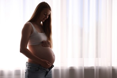 Photo of Beautiful pregnant woman near window at home. Space for text