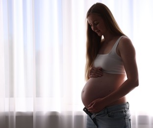 Photo of Beautiful pregnant woman near window at home. Space for text