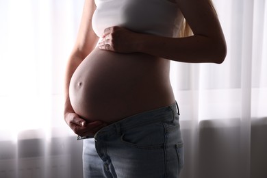Photo of Beautiful pregnant woman near window at home, closeup