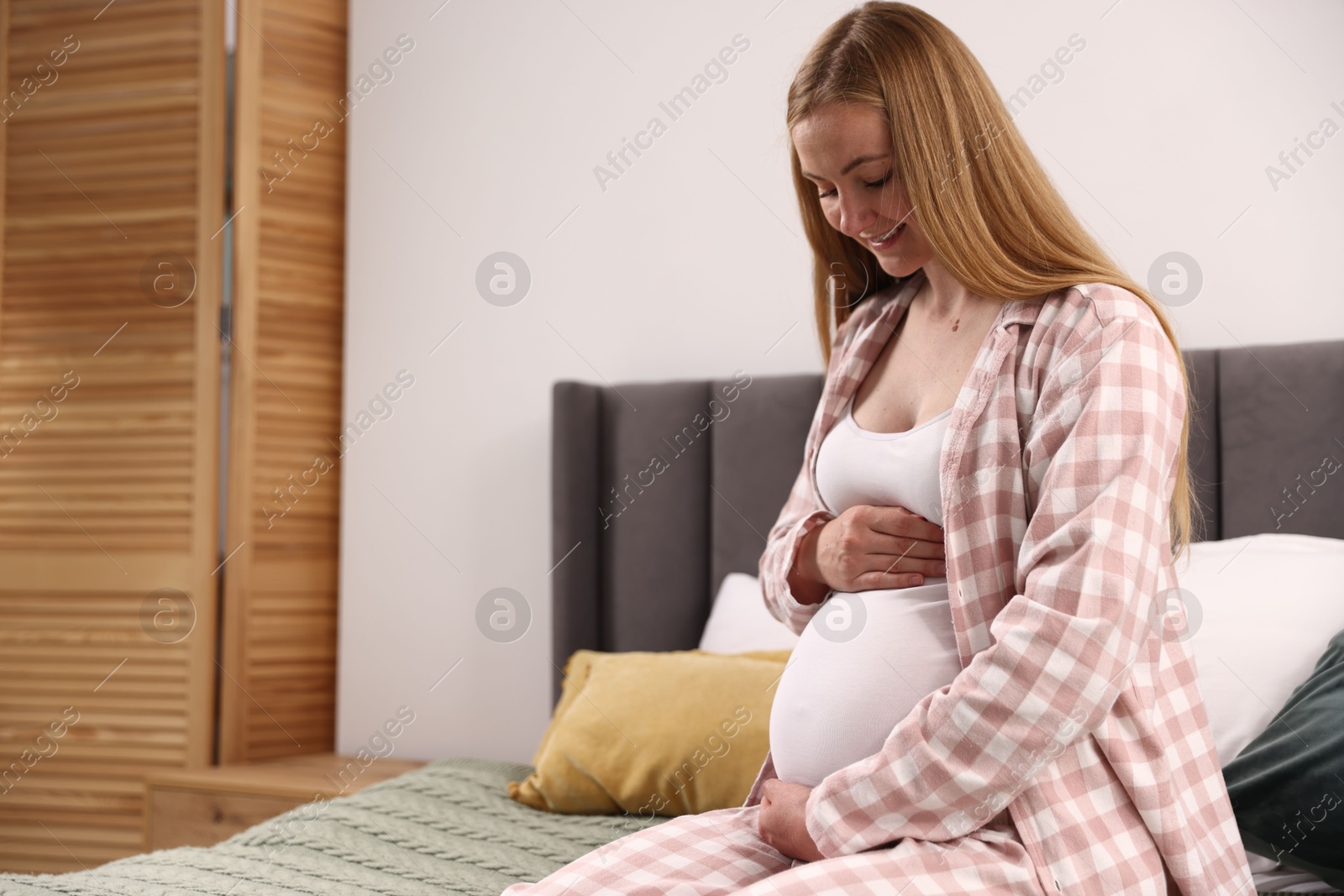 Photo of Beautiful pregnant woman on bed at home. Space for text