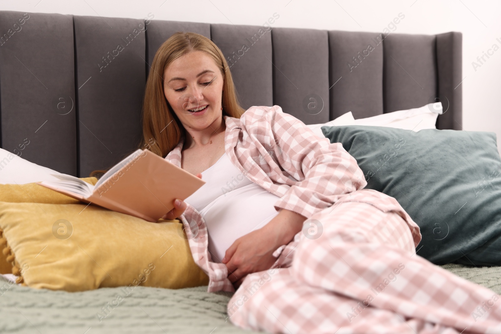 Beautiful pregnant woman reading book on bed at home Photo of Beautiful pregnant woman reading book on bed at home