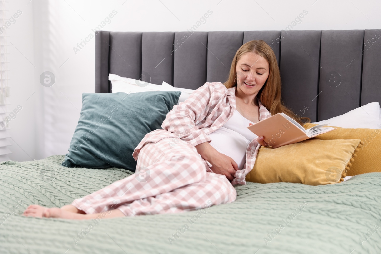 Photo of Beautiful pregnant woman reading book on bed at home